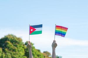 mãos mostrando arco-íris lgbtq e bandeira da Jordânia no fundo da natureza. apoiar a comunidade de lésbicas, gays, bissexuais, transgêneros e queer e o conceito de mês do orgulho foto