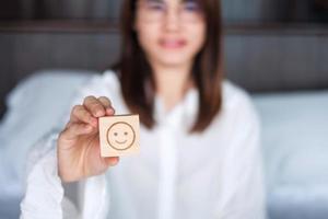 mulher feliz segurando o bloco de rosto de emoção de sorriso. cliente escolhe emoticon para comentários de usuários. classificação de serviço, saúde mental, pensamento positivo, satisfação, avaliação e conceito de feedback foto