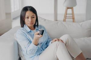 mulher espanhola entediada segurando o controle remoto e assistindo filme ruim na tv e muda os canais. foto