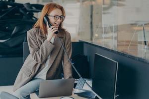 mulher de óculos falando ao telefone enquanto está sentado em seu local de trabalho no escritório foto