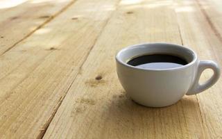 uma xícara de café preto em uma prancha de madeira foto