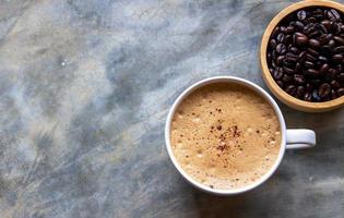 xícara de cerâmica branca de café mocha em uma mesa de concreto perto de uma tigela de madeira de grãos de café. foco seletivo de uma xícara de café foto