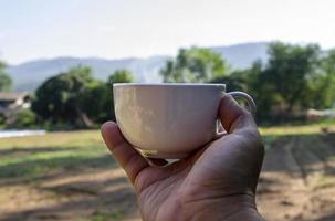 conceito criativo de bebidas de refresco matinal de uma mão de homem segurando uma xícara de café com terras agrícolas em um campo de fundo da tailândia foto