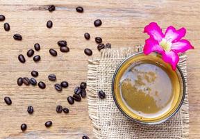 vista iop de uma xícara de café americano preto em uma mesa de madeira de saco com uma pilha de grãos de café marrons orgânicos. conceito de refresco matinal foto