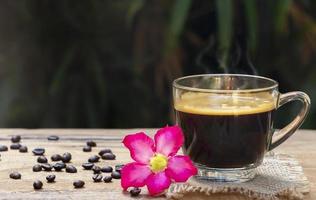 xícara de café americano preto quente com fumaça agradável acima de uma xícara em um saco e mesa de madeira em um fundo natural. bom dia com um conceito de bebidas refrescantes foto