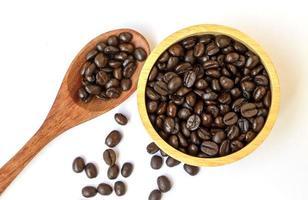 grãos de café arábica torrado marrom orgânico em uma tigela de madeira e colher em fundo branco. concentre-se em grãos de café em uma tigela. feijão de café famoso e de boa qualidade de chiangmai, tailândia foto