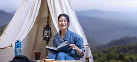 mulher asiática lendo livro enquanto em um acampamento de trekking solo no topo da montanha com pequena barraca para atividades de fim de semana e perseguição ao ar livre foto