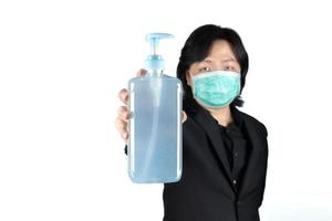 homem asiático está segurando e mostrando a limpeza de gel de álcool na mão e usa máscara em fundo branco claro. foto