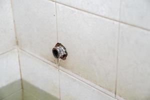 cano quebrado na parede de azulejos do banheiro. foto