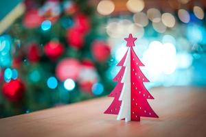 decoração de árvore de natal de plástico vermelho e branco na mesa de madeira com borrão grande árvore de natal atrás. foto