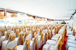 tenda interna temporária de ar condicionado para eventos ao ar livre durante o dia. dentro das barracas tem tapete vermelho e muita cadeira coberta por pano branco e fita dourada. foto