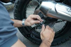 feche a mão do trabalhador técnico, roda de moto fixa na parte externa da garagem. foto