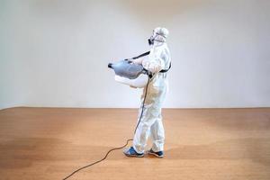 homem técnico profissional em traje de prevenção pulveriza solução esterilizante por máquina de pulverização elétrica em piso de madeira e fundo branco com luz de estúdio. foto