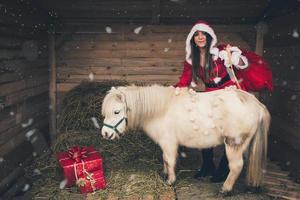 uma mulher de natal com presentes e um cavalo branco foto