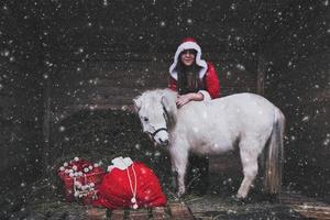 uma mulher de natal com presentes e um cavalo branco foto