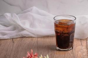 bebida de cola cola com gelo em vidro colocado em fundo de madeira foto