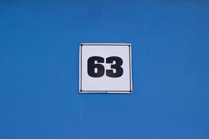 placa de metal com casa número 63 cor preta no branco. em uma parede azul. a parede da casa foto