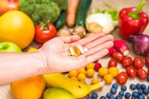mão segurando suplementos alimentares sobre legumes e frutas para um estilo de vida saudável foto