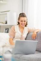 dona de casa jovem feliz usando o laptop na sala de estar foto