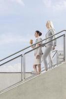 Vista lateral de mulheres de negócios descendo escadas contra o céu foto
