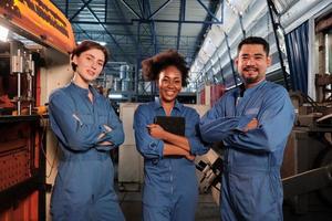 trabalhadores alegres da indústria multirracial em uniformes de segurança se alinham e braços cruzados juntos após o sucesso do trabalho e expressam sorrisos e felicidade na fábrica mecânica. profissão de engenheiro. foto