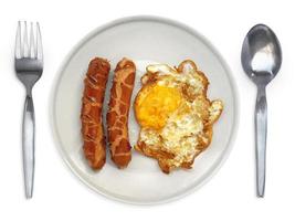 ovo frito em um prato com salsicha de garfo e colher em um fundo branco foto