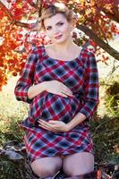 menina grávida está usando vestido xadrez no parque