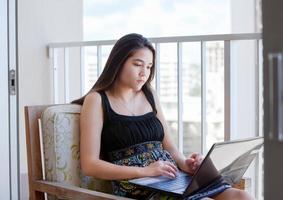 menina adolescente biracial no pátio alto com computador portátil foto