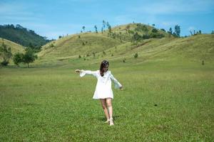 linda garota de pé e agindo na frente da montanha careca ou phu khao ya com campo de grama verde e céu azul. uma das atrações naturais de viagem na província de ranong, tailândia foto