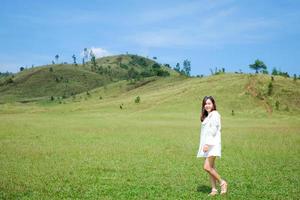 linda garota de pé e agindo na frente da montanha careca ou phu khao ya com campo de grama verde e céu azul. uma das atrações naturais de viagem na província de ranong, tailândia foto