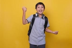 estudante asiático em estilo casual usa mochila preta e fone de ouvido contra fundo amarelo. de volta à escola e ao conceito de dia das crianças. foto