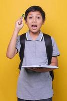 menino de escola asiático com uma expressão quando ele tem uma ideia ou solução, vestindo camisa polo cinza e segurando livro e caneta. de volta ao conceito de escola. foto