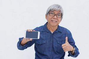 retrato de homem maduro asiático em estilo casual jeans segurando smartphone, mostrando a tela e o polegar para cima - estilo de vida e conceito sênior de rede social e online foto