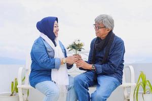 casal de idosos asiáticos. alegre bom casal romântico sênior está sentado e rindo um ao outro enquanto mantém juntos a flor branca artificial. foto