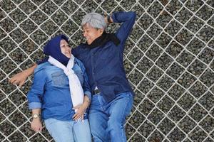 retrato de casal romântico de idosos asiáticos deitado na rede relaxante e olhando um ao outro com sorriso de felicidade foto