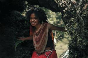 exótica jovem papua da tribo dani em roupas tradicionais com coroa de penas está sorrindo e brincando na caverna foto