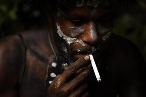 close-up do rosto pintado dani tribo papua homem está fumando um cigarro. foto