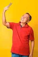 feliz homem sênior asiático tomando selfie usar smartphone. 60 anos aposentados maduros desfrutando de videochamada de reunião virtual, bate-papo, conversando, olhando para smartphone em fundo amarelo. foto