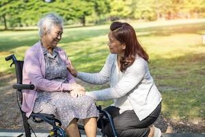 cuidador ajuda e cuida paciente idosa asiática ou idosa sentada e feliz na cadeira de rodas no parque, conceito médico forte e saudável. foto