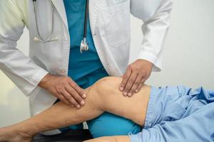 Médico fisioterapeuta examinando, massageando e tratando o joelho e a perna do paciente sênior no hospital de enfermagem da clínica médica ortopedista. foto