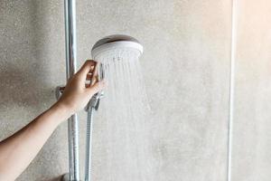mão segurando o chuveiro durante o banho com fundo de parede no banheiro moderno foto