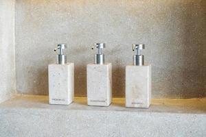 garrafas de produtos de higiene pessoal no banheiro do hotel de luxo ou casa moderna. conjunto de recipientes de banho, gel de banho corporal, xampu e condicionador de cabelo em cerâmica com fundo de parede foto