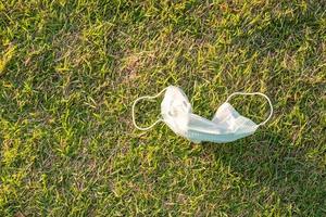 resíduos de máscara cirúrgica descartável na grama durante a pandemia de covid-19. contaminação, poluição ambiental e plástica. lixo na praia efeito na saúde dos oceanos e animais foto