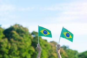 mão segurando a bandeira do brasil sobre fundo de céu azul. dia da independência de setembro e conceitos de celebração feliz foto