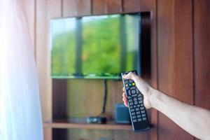 mão usando o controle remoto para ajustar a tv inteligente dentro da sala moderna em casa ou hotel de luxo foto