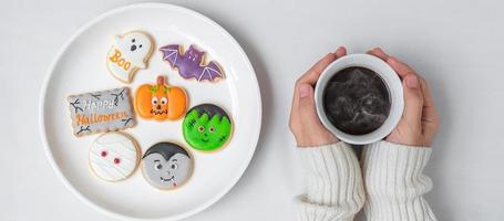 mão de mulher segurando a xícara de café durante a ingestão de biscoitos engraçados de halloween. feliz dia das bruxas, truque ou ameaça, olá outubro, outono outono, conceito tradicional, festa e feriado foto