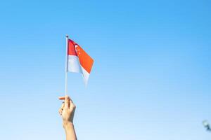 mão segurando a bandeira de Cingapura no fundo do céu azul. dia nacional de singapura e conceitos de celebração feliz foto