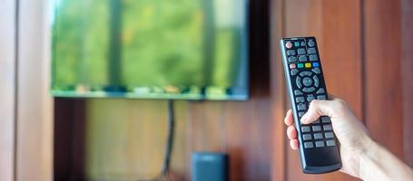 mão usando o controle remoto para ajustar a tv inteligente dentro da sala moderna em casa ou hotel de luxo foto