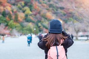 turista de mulher feliz tirando fotos coloridas deixa montanhas pela câmera em arashiyama, jovem viajante asiático visita em kyoto, japão. outono outono temporada, férias, férias e conceito de turismo