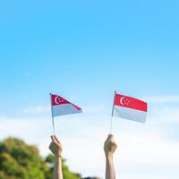 mão segurando a bandeira de Cingapura no fundo do céu azul. dia nacional de singapura e conceitos de celebração feliz foto